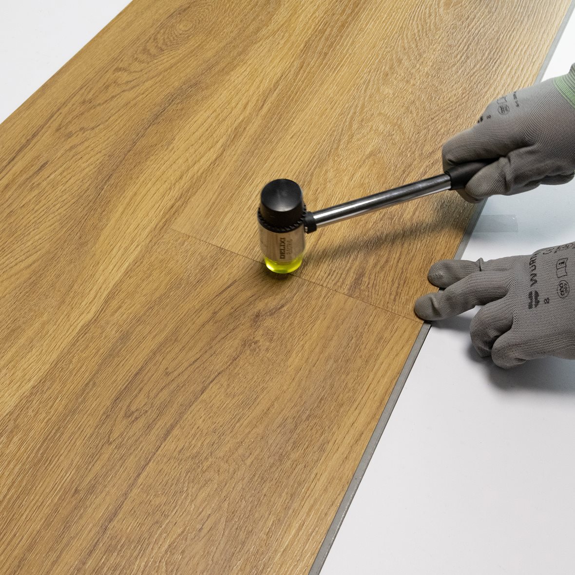 Pontillisen vinyylilankun asennus. Lankkujen lyhyen sivun pontit viedään kohdikkain ja lukitaan kumivasaran napautuksella.