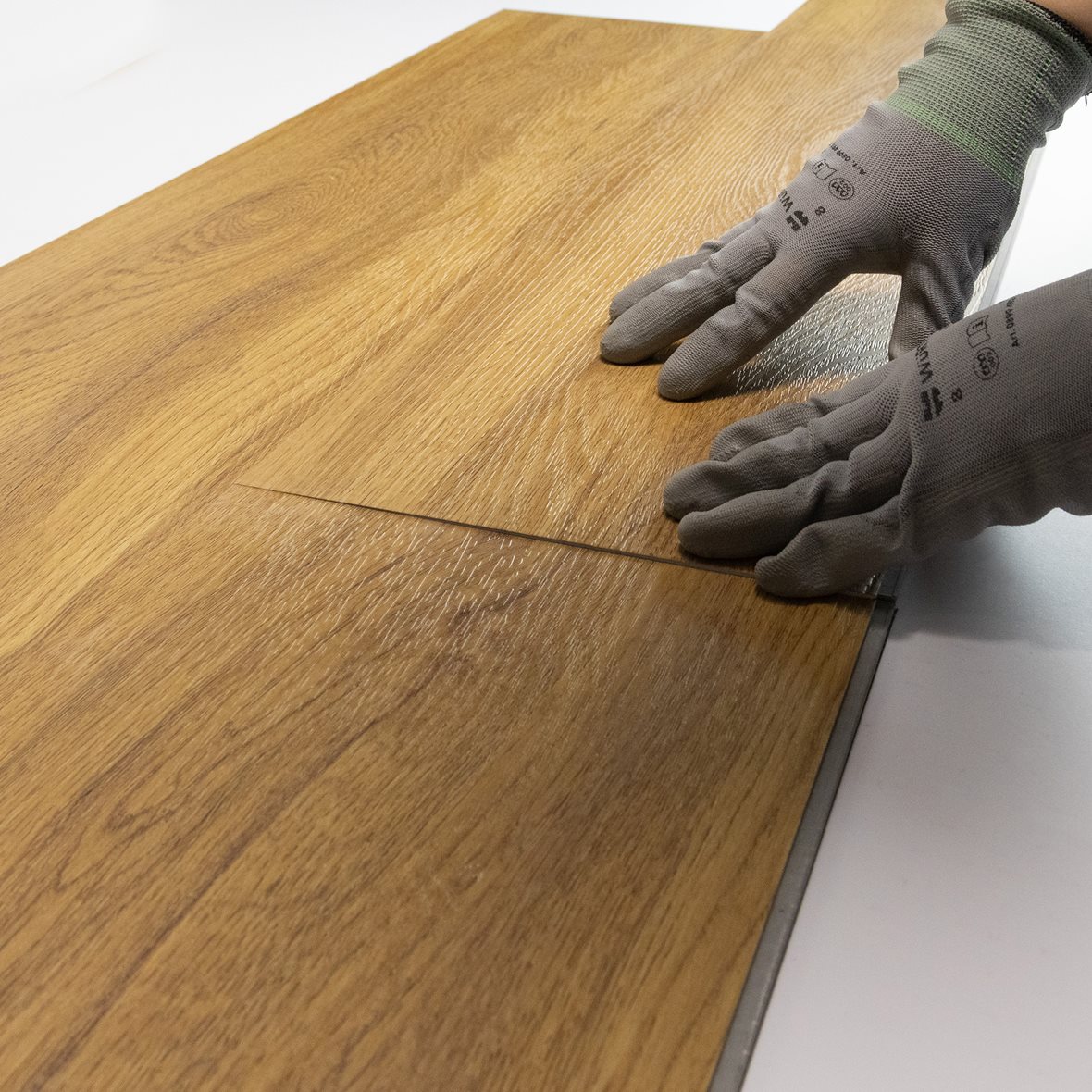 Pontillisen vinyylilankun asennus. Pitkän sivun pontin kiinnityksen jälkeen lankku painetaan varovasti tasaiseksi niin että lyhyen sivun pontti kiinnittyy.